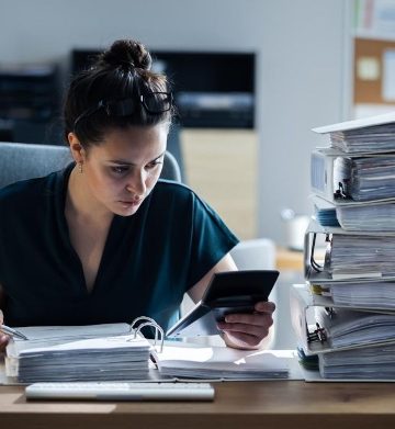 Young,Businesswoman,Working,At,Office,With,Stack,Of,Folders,On